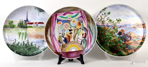 Lotto di tre piatti dipinti a mano, con decori raffiguranti paesaggi e scena di teatro, XX secolo, diam. max cm 29.