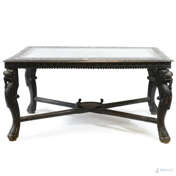 Tavolo coloniale in legno ebanizzato, intagliato a motivi vegetali, con quattro gambe a foggia di fiere  [..]