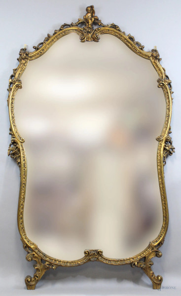 Grande specchiera in legno intagliato e dorato, metà XX secolo, cornice di linea sagomata scolpita a volute, sormontata da amorino, cm h 200x120