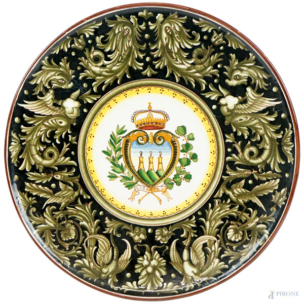 Grande piatto in maiolica smaltata policroma con decoro centrale raffigurante stemma della città di S. Marino, tesa a grottesche, diam.cm 45,5, firmato sotto la base