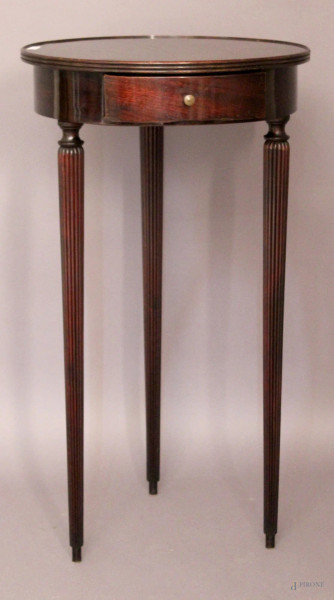 Tavolino d&#39;appoggio di linea tonda in mogano ad un cassetto, poggiante su tre gambe a colonne scanalate, XX sec., H 78 cm, diametri 43 cm.