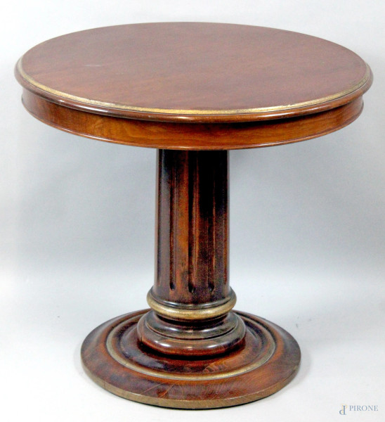Tavolino di linea tonda in legno tinto a noce con particolari dorati, poggiante su colonna scanalata, altezza 66 cm, diametro 71,5 cm.
