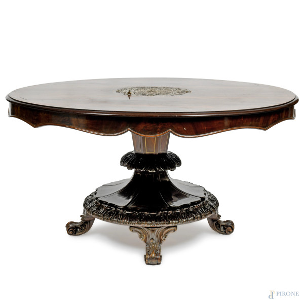Tavolo circolare in legno scuro con piano a decoro centrale in lamina di metallo su base dal fusto conico poligonale terminante in pedana circolare intagliata su quattro piedi a ricciolo, XX secolo, cm 73x133, (graffi, difetti, segni di usura)