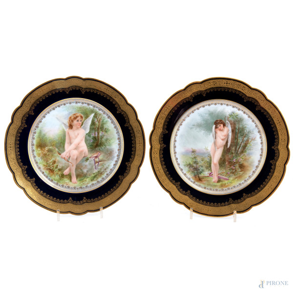 Coppia di piatti in porcellana nei toni del blu e dell'oro con raffigurazioni di putti al cavetto, XX secolo, diametro cm 25, (lievi segni di usura)