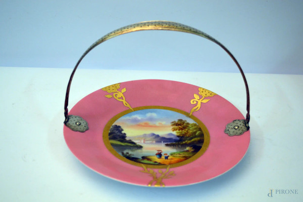 Piatto di linea tonda in porcellana con medaglione centrale a decoro policromo di paesaggio fluviale con figure, particolari dorati su fondo rosa, manico in argento, diam. 25 cm.