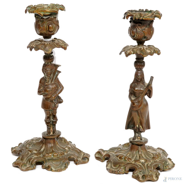 Coppia di candelieri in bronzo cesellato a rigogliosi motivi fogliacei e fusti a foggia di figure musicanti, XX secolo, altezza cm 19,5, (difetti, mancanze)