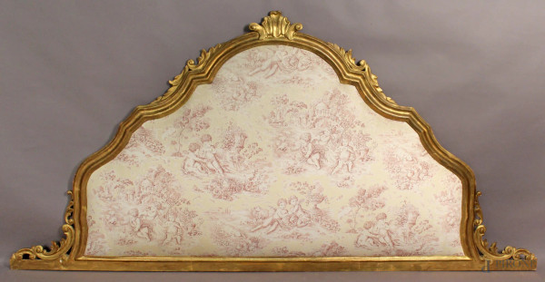 Testata da letto in legno intagliato e dorato a motivi di fiori d&#39;acanto, rivestita in tessuto a motivi di putti, XIX sec, h.11x229 cm.