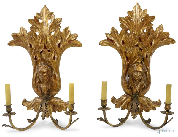 Coppia di appliques a due luci, XIX secolo, in legno dorato, intagliato e scolpito a motivo di teste femminili e foglie d'acanto, due bracci in metallo dorato, cm 69x41, (difetti).