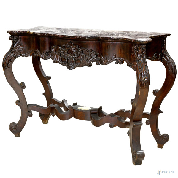 Consolle Luigi Filippo con piano in marmo, impiallacciata in mogano con profilo mosso riccamente intagliato al centro e agli angoli,  poggiante su quattro gambe mosse raccordate  e terminanti a ricciolo, XIX secolo, cm 98x133x48, (rottura del piano, difetti)