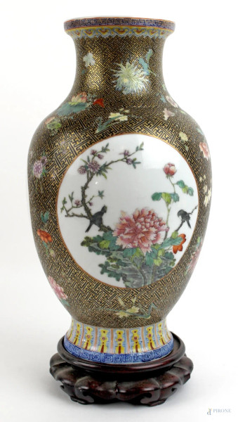 Vaso in porcellana policroma, decorato con due riserve raffiguranti rami fioriti e volatili, altezza cm. 30, poggiante su base in legno, Cina, XX secolo.