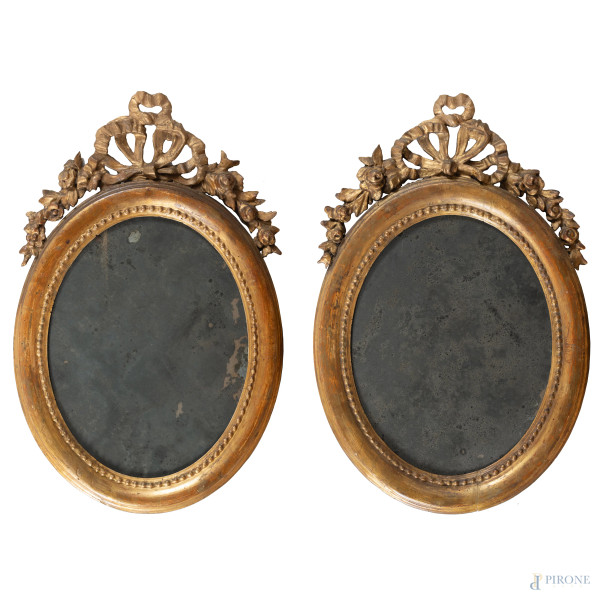 Coppia di specchiere a serto ovale in legno intagliato e dorato, XX secolo, cm 64x40, (segni di usura, fori di tarlo, scalfiture, difetti)