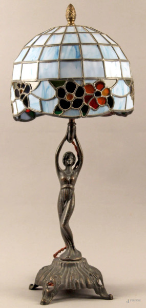Lampada da tavolo stile tiffany, base sorretta da figura in bronzo, paralume in vetro piombato, h. 63 cm.