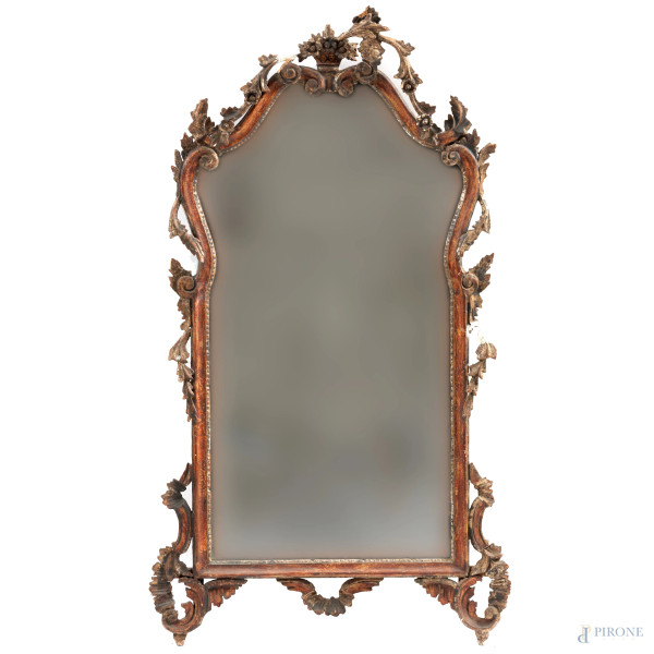Specchiera in legno intagliato e dorato a volute vegetali e floreali, XX secolo, cm 127x65, (segni di usura, perdita di doratura, rotture, mancanze, restauri, difetti)