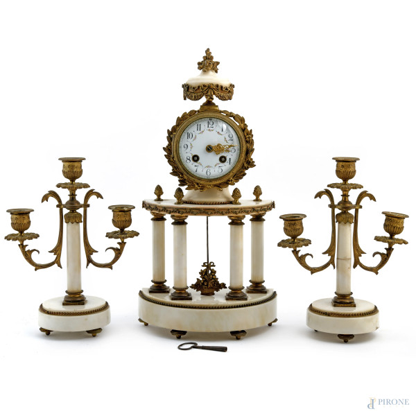 Trittico composto da orologio e coppia di candelieri a tre fuochi in bronzo e marmo. Quadrante smaltato in ceramica con lancetta in bronzo dorato riccamente cesellata e numeri arabi. XX secolo, altezza massima cm 41,5, (scalfiture, segni di usura, da revisionare)