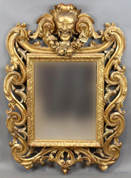 Specchiera in legno intagliato e dorato, cornice a volute e foglie d'acanto, cimasa con mascherone e festone, ingombro cm h112x80, luce cm 52x41, XIX secolo, (difetti).