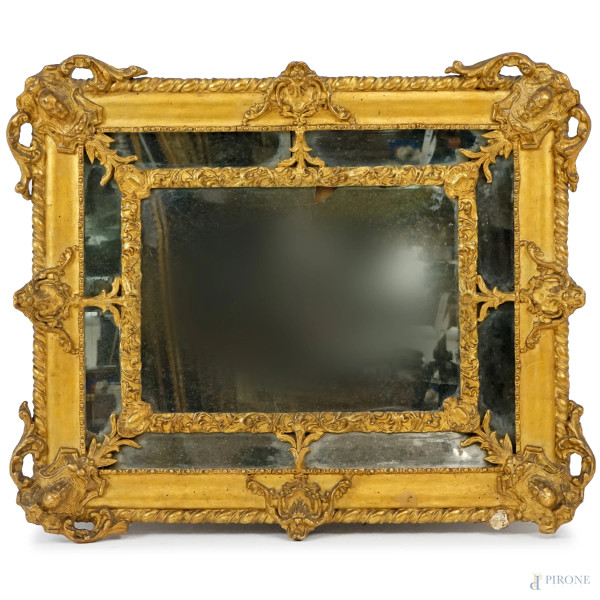 Specchiera in legno intagliato e dorato, inizi XX secolo, cornice scolpita a motivi fogliacei e testine ai quattro angoli, cm 73x87, (difetti)