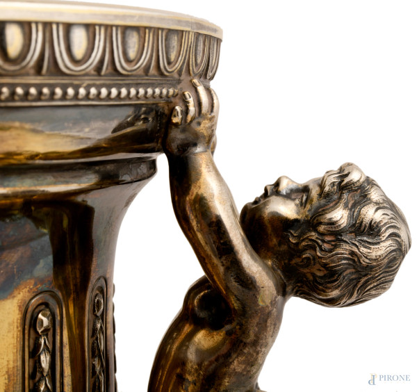 Grande vaso biansato in argento con prese a guisa di putti su foglie d'acanto a sorreggere l'orlo...