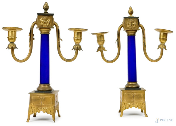 Coppia di candelabri a due luci in metallo dorato e cesellato, fusto a colonna in vetro blu, inizi Xx secolo, cm h 32