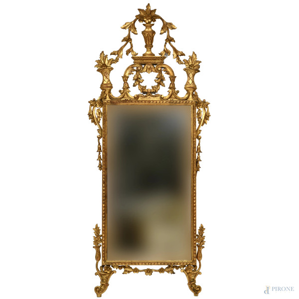 Specchiera in legno dorato e finemente intagliato a volute e girali con elemento apicale composto a motivi vegetali, XX secolo, cm 188x78, (scalfiture, piccole cadute di dorature, segni del tempo)
