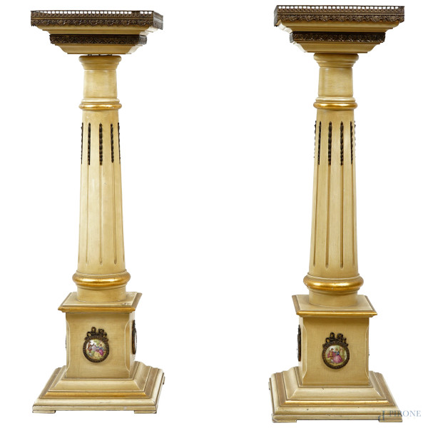 Coppia di colonne in legno laccato bianco, con applicazioni in metallo brunito e quattro placchette ovali in porcellana policroma, manifattura del XX secolo, cm h 99, (difetti)