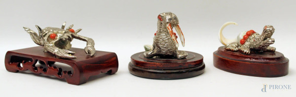 Lotto composto da tre sculture in metallo argentato e conchiglia con filo in corallo a soggetto di coccodrillo, tricheco e scorpione, poggianti su basi in tek, H massima 8 cm.