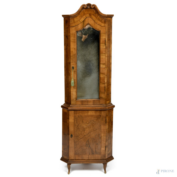 Angoliera a doppio corpo in legno impiallacciato in varie essenze con corpo inferiore a singola anta e corpo superiore specchiato con elemento apicale intagliato a volute, XX secolo, cm 178x58x35, (segni di usura, scalfiture, difetti)