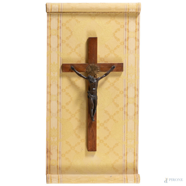 Crocifisso in bronzo su croce in legno applicata su pannello rivestito in tessuto, XX secolo, misure complessive cm 83x42, (segni di usura, rotture, restauri, difetti)