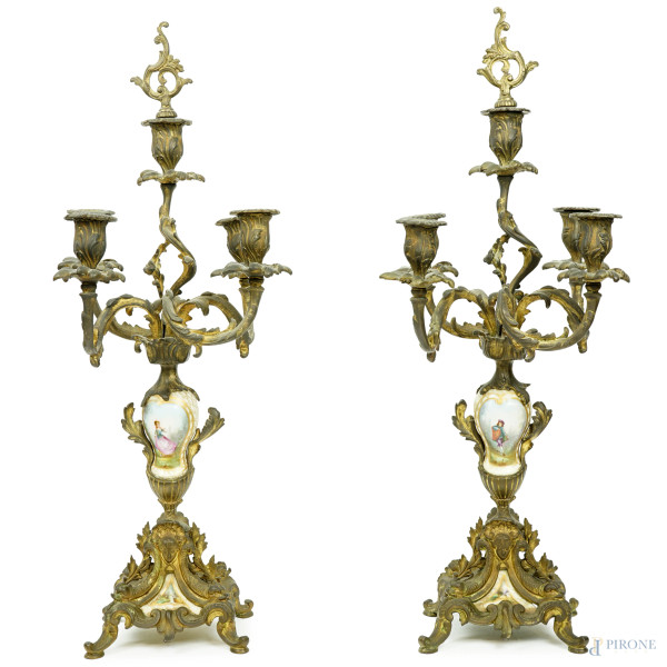 Coppia di candelabri a cinque fiamme in bronzo e porcellana, Francia, fine XIX-inizi XX secolo, cinque braccia a ramages, fusto e base con applicazioni in porcellana raffiguranti gentiluomo e nobildonna entro paesaggi, cm h 60, (difetti)