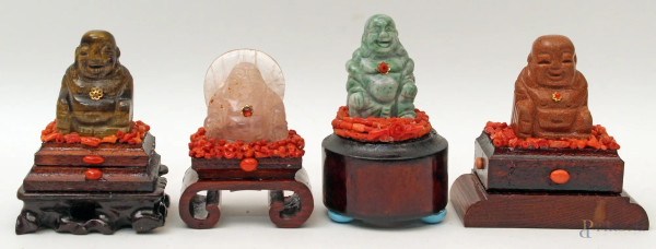 Lotto composto da quattro Budda diversi in pietre dure, contornate da coralli, poggianti su basi in legno, H 8 cm.