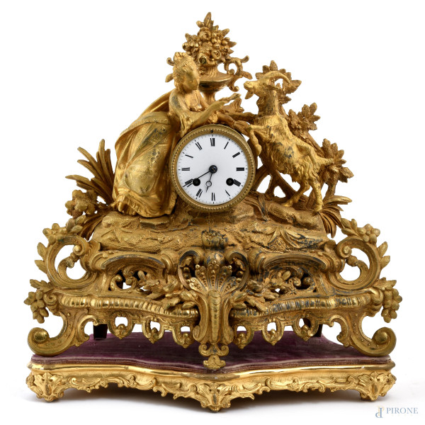 Orologio in antimonio dorato con quadrante a smalto e numeri romani. Sculture apicali di dama con capra e preziose volute vegetali e floreali. XX secolo, cm 38x41x12 (misure senza campana), (difetti, da revisionare)