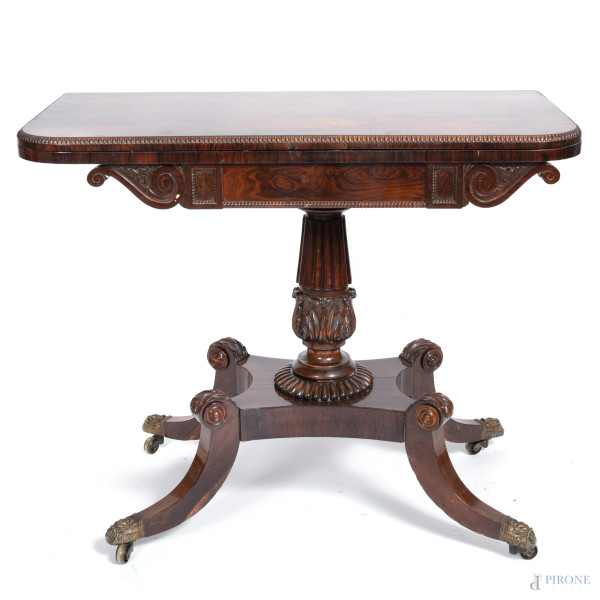 Tavolino da gioco in legno impiallacciato poggiante su fusto intagliato sostenuto da pedana sagomata terminante quattro gambe arcuate con rotelle, XIX secolo, cm 73x91,5x90,5 (aperto); cm 75x91,5x45,5 (chiuso), (segni di usura, scalfiture, graffi)