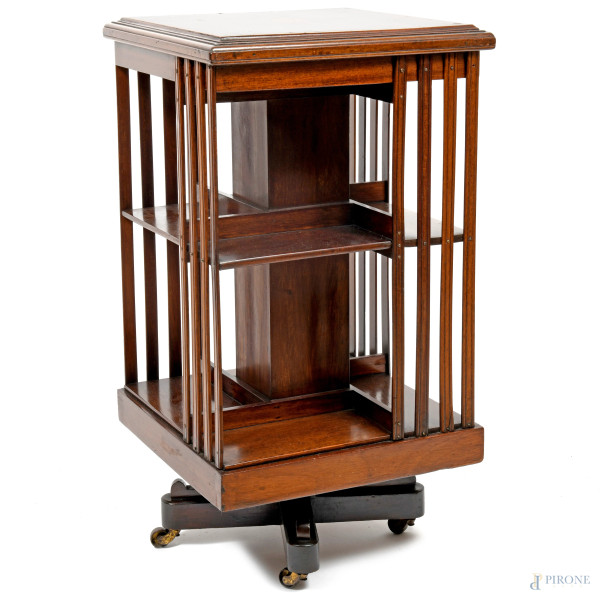 Libreria girevole in legno di noce con struttura parallelepipeda a doppio ripiano, raccordato da listelli, poggiante su basamento munito di rotelle. Piano con intarsio centrale. XX secolo, cm 89x47x47, (difetti)