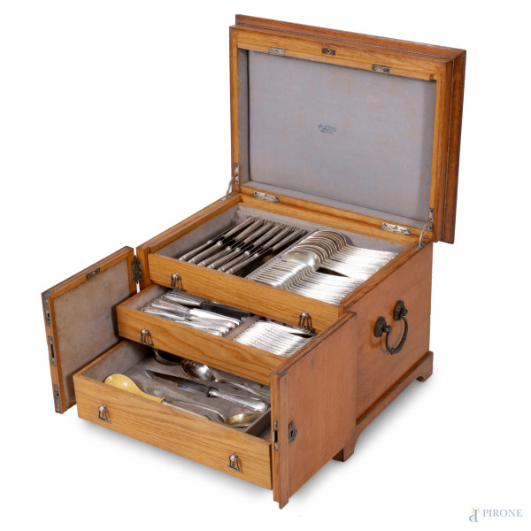 Posate in metallo argentato entro mobiletto in rovere a doppia anta celante tre cassetti in colonna