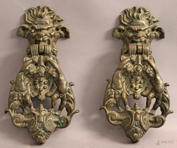 Coppia di battiporta in bronzo lavorato raffiguranti mascheroni e putti, H 28 cm.