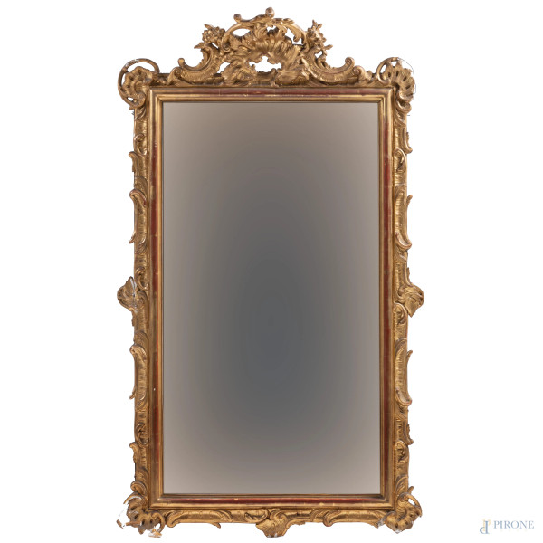 Specchiera in legno intagliato e dorato a volute vegetali e floreali, XX secolo, cm 143,5x81, (segni di usura, perdita di doratura, rotture, mancanze, restauri, difetti)