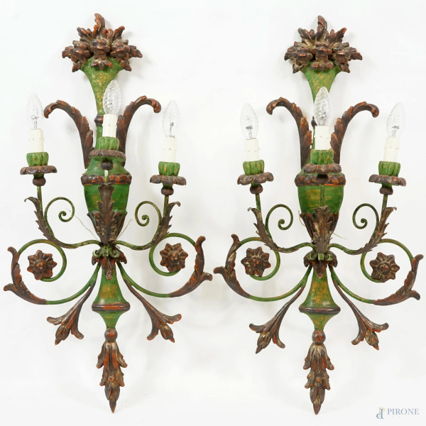 Coppia di appliques a tre bracci, in legno policromo nei toni del verde, dell'oro e del bruno, intagliato con cartella a foggia di vaso  coronato da fiori e irradiante racemi, XX secolo, cm 79x42, (difetti)