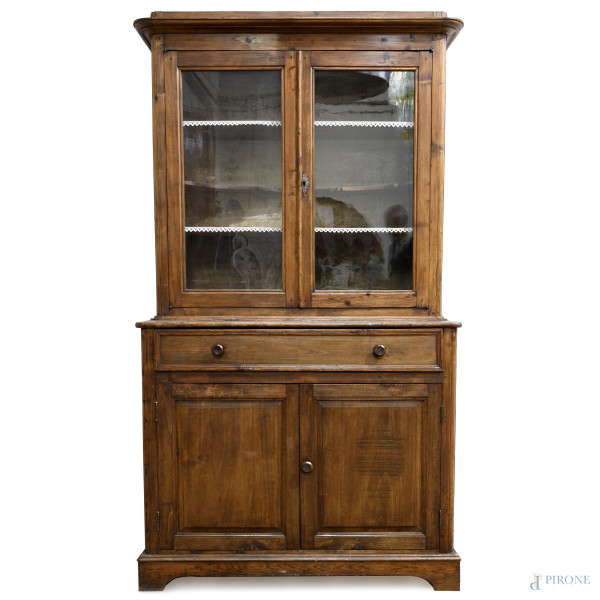 Credenza in legno dolce con corpo inferiore scandito da cassettone e doppia anta, corpo superiore...