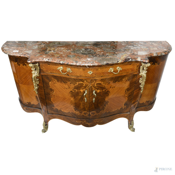 Servante in legno impiallacciato e intarsiato in varie essenze con piano sagomato in marmo. Fronte mosso scandito da due ante convesse laterali che incorniciano un cassettone e un vano a doppia anta centrali. Ferramenta e inserti in bronzo dorato. XX secolo, cm 104x202x63, (graffi, segni di usura, difetti)