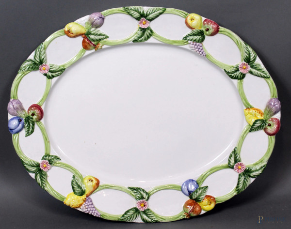 Grande piatto in ceramica smaltata di linea ovale, bordo con decori policromi a fiori e frutti, cm. 51x41, XX secolo.