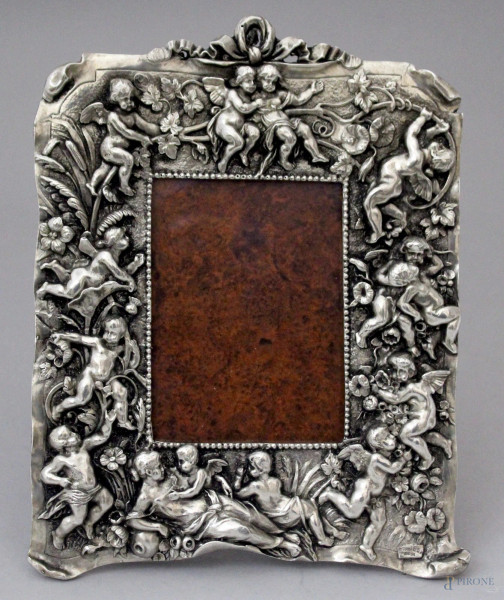 Cornice portafoto in metallo argentato a decoro di putti a rilievo, XX secolo, misure ingombro altezza 27x20,5 cm.