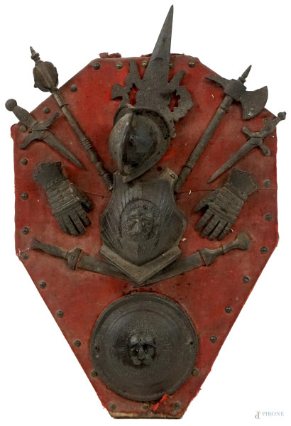 Trofeo con elementi di armatura, XIX secolo,  pannello in legno a forma di scudo rivestito in stoffa rossa, ingombro max cm 50x35, (difetti).