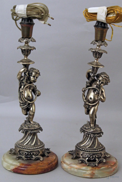 Coppia candelieri ad una luce in metallo argentato retti da putti, basi in onice, completi di paralumi, h. 35 cm