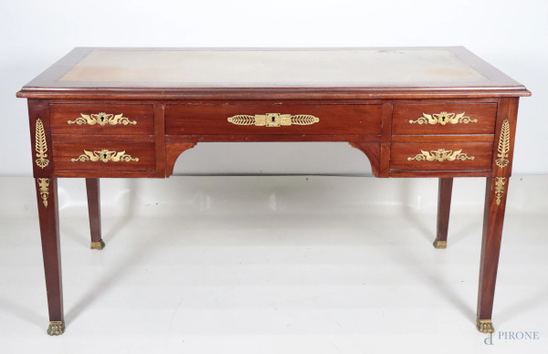 Scrivania in mogano con guarnizioni e fregi in bronzo dorato. Piano in pelle goffrata e cinque cassetti al fronte, XIX-XX secolo, cm 79x146x75, (segni di usura, scalfiture, graffi, difetti)