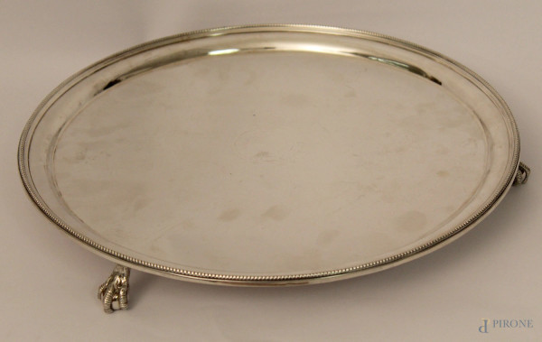 Piatto di linea tonda in argento, poggiante su tre piedini a zampe d'aquila, XIX sec., gr. 1280, diam. cm 35.