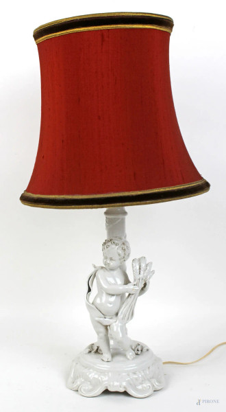 Lampada da tavolo in porcellana bianca con putto, completa di paralume in stoffa rossa, altezza cm. 48, marcata La Diana, Vecchia Bassano, XX secolo.