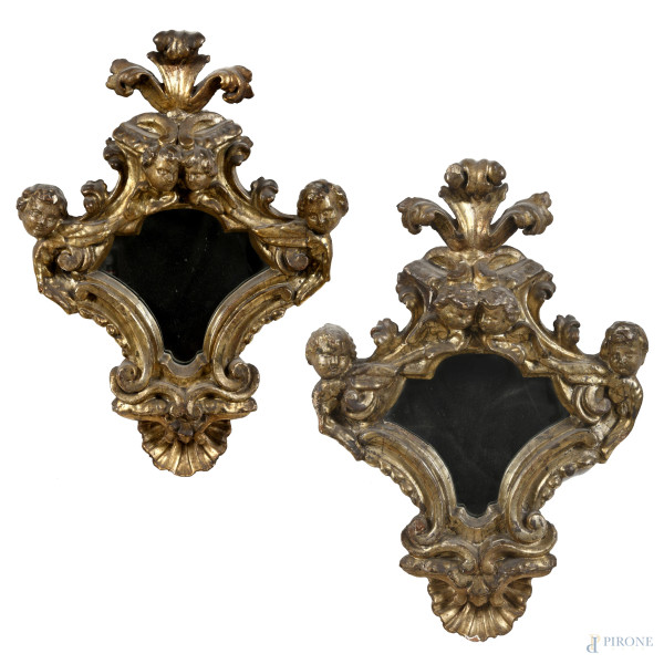 Coppia di specchierine in legno dorato ed intagliato a volute e teste di cherubini, XVII-XVIII secolo, cm 58x44; luce cm 20x21, (segni di usura, difetti, scalfiture, rotture, mancanze)