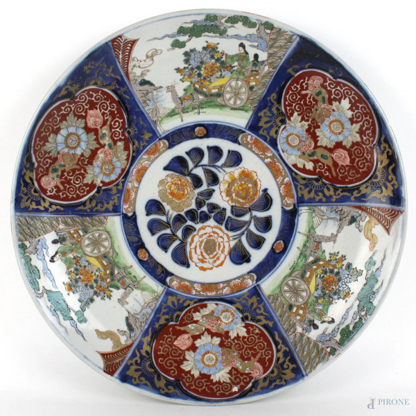 Piatto in porcellana Imari, a decoro di fiori e paesaggi con carretti e figure, diametro cm. 46, Giappone, XX secolo.