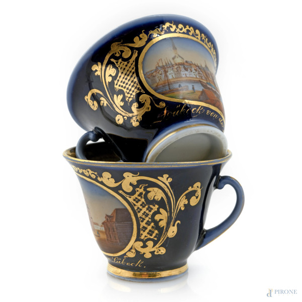Lotto composto da due tazzine in porcellana tedesca nei toni del blu e dell'oro con vedute di città, XX secolo, altezza cm 6,5, (segni di usura, difetti)
