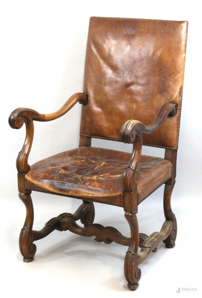 Poltrona in noce, inizi XX secolo, in legno intagliato, seduta e schienale in pelle, braccioli a ricciolo, cm h 108, (difetti alla seduta).