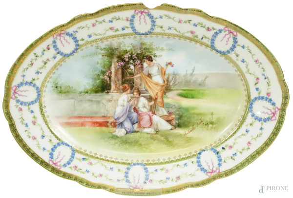 Piatto ovale in porcellana policroma con scena neoclassica, bordo decorato con ghirlande e swag con fiori blu e rosa, marchio sul retro, Francia, inizio XX secolo, cm 31,3x21 (difetti)